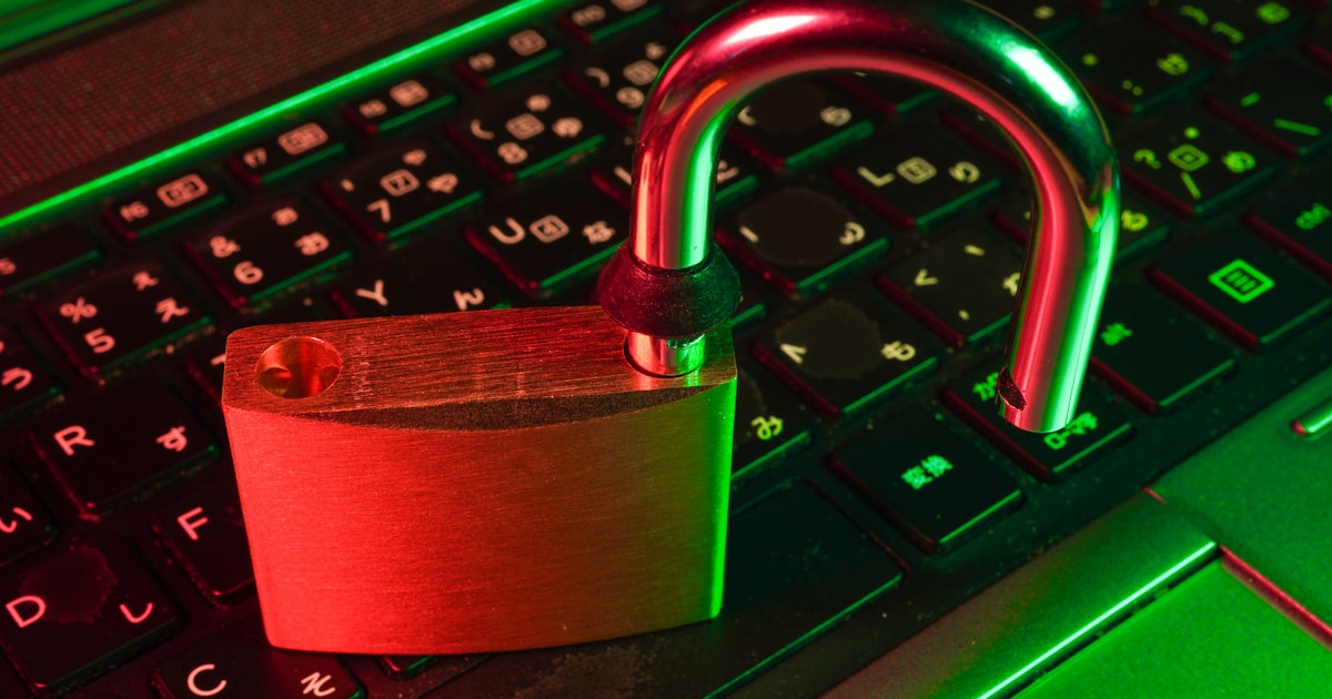 An open padlock sitting on a backlit laptop keyboard with red and green lighting — symbolizing a compromised website